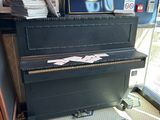 un piano dans un coin d'une pièce où sont accrochés des tableaux au mur