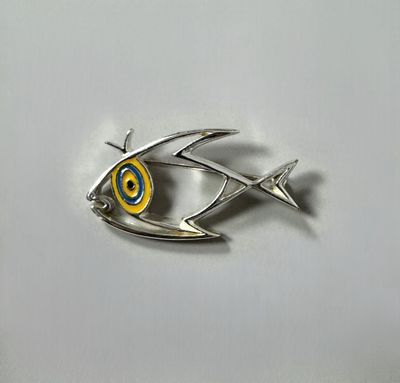 a close up of a fish shaped broochle on a white surface