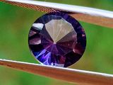 une image montrant un gros plan d'un diamant violet tenu par une paire de pinces
