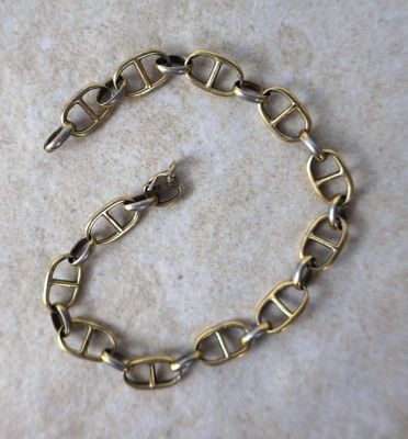 un gros plan d'un bracelet à chaîne en or posé sur une surface en marbre