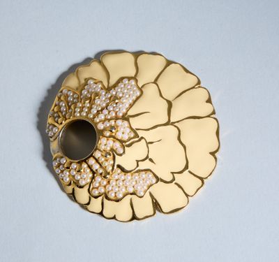 une broche en or ornée de perles, posée sur un fond blanc