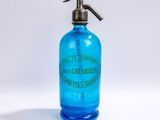 une bouteille en verre bleue munie d'une poignée en métal, posée sur une surface blanche