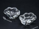 pair of clear glass ashtrays with a spoon and spoon rest on a black background