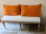 two orange pillows on a white bench next to a wall
