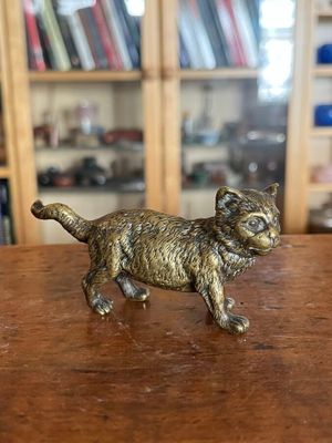figurine en laiton représentant un chat, posée sur une table devant une bibliothèque