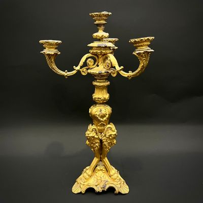 un chandelier ancien en laiton à trois bougies, posé sur un socle