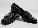 une paire de chaussures en cuir noir ornées de boucles, posées sur une surface blanche