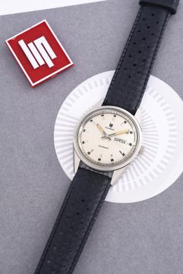 une montre posée sur un morceau de papier, à côté d'une épingle