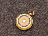 une image représentant une montre de poche en or posée sur un tissu gris