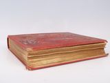 an old book with a red cover sitting on a white surface