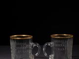 two clear glass cups with gold rims on a black surface