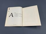 un livre ouvert sur lequel figure l'image en noir et blanc d'une lettre