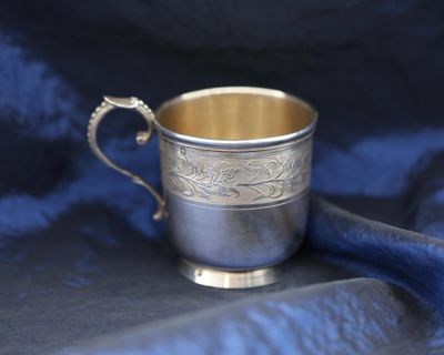 a silver cup with a handle on a blue cloth