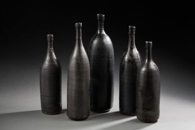 quatre bouteilles noires sont alignées sur une surface blanche