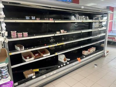 de nombreuses étagères vides dans une épicerie, sur lesquelles se trouvent des produits alimentaires