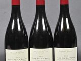 three bottles of red wine are lined up on a gray surface