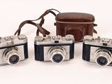 three old cameras are sitting next to each other on a white surface