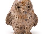 une petite figurine de chouette posée sur une surface blanche