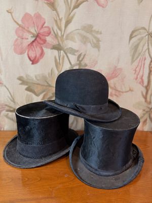 deux chapeaux haut-de-forme noirs posés sur une table en bois devant un papier peint à motifs floraux