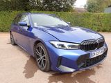 Une berline BMW Série 3 garée dans un parking, avec des buissons en arrière-plan