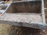 un évier en béton posé à même le sol, à côté d'un tas de pierres