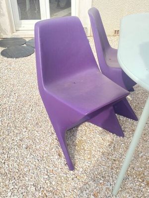 deux chaises violettes et une table à l'extérieur, sur le gravier