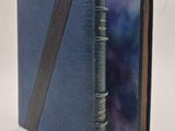 un livre bleu orné d'une bande noire est ouvert sur une surface blanche