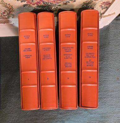 trois livres orange posés sur un canapé, à côté d'un fauteuil