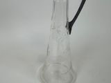 a clear glass pitcher with a black handle on a white table