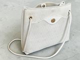 beige and white purse on concrete floor with handle and strap