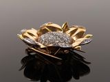 an image of a gold and diamond flower broochle on a reflective surface