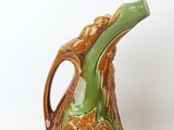 a brown and green vase with a handle on a white surface