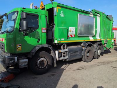 a green garbage truck that is parked in a lot