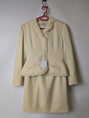une robe et une veste beiges ornées de dentelle, suspendues à un cintre au mur