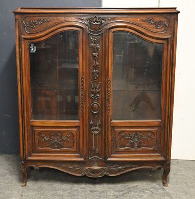 une armoire ancienne en bois, dotée de portes vitrées et ornée de sculptures sur les portes