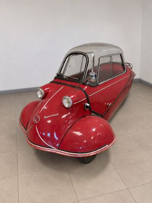 Une vieille voiture rouge est garée dans une pièce au sol carrelé.