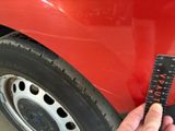 a person holding a measuring ruler next to a red car