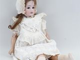 an antique porcelain doll sitting on the ground wearing a white dress and bonnet