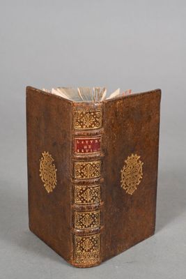an old book with a red cover sitting on top of a table
