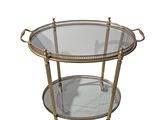 a round glass and brass serving cart with two trays