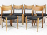 four wooden chairs with black leather seats against a white wall