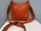 an orange purse with a colorful strap sitting on top of a white table