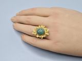 someone is holding a ring with a green stone on it