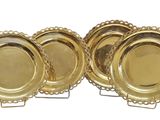 quatre assiettes en or aux bords festonnés, posées sur des socles, sur un fond blanc