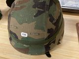 un casque de camouflage posé sur une table à côté d'une paire de ciseaux