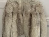 une veste en fourrure blanche suspendue à un cintre en bois devant une porte
