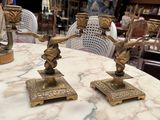 two brass candles on a marble table with a woman in the background