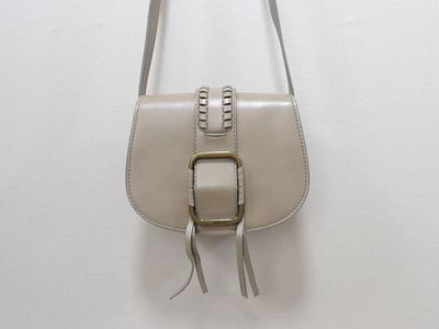 beige leather handbag with silver hardware and tassels hanging on a white wall