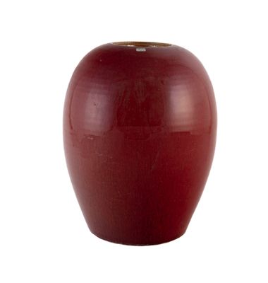 un vase rouge posé sur une surface blanche