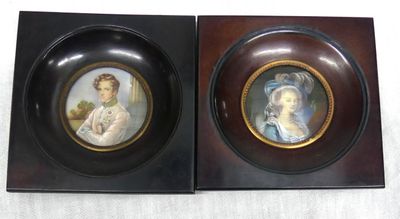 two framed pictures of women in formal dress sitting on a table
